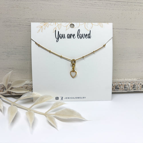 Itsy gold heart necklace with a resin filled white center on a card with 'You are loved'