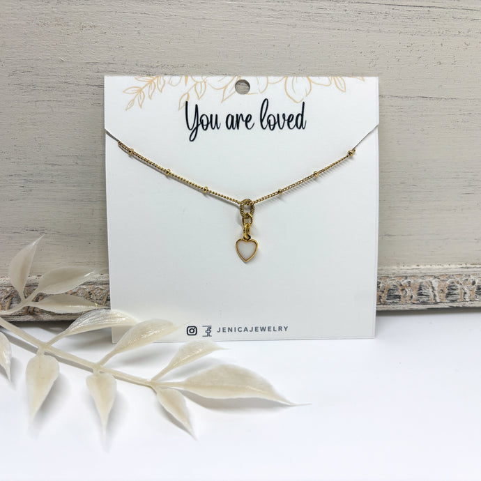 Itsy gold heart necklace with a resin filled white center on a card with 'You are loved'