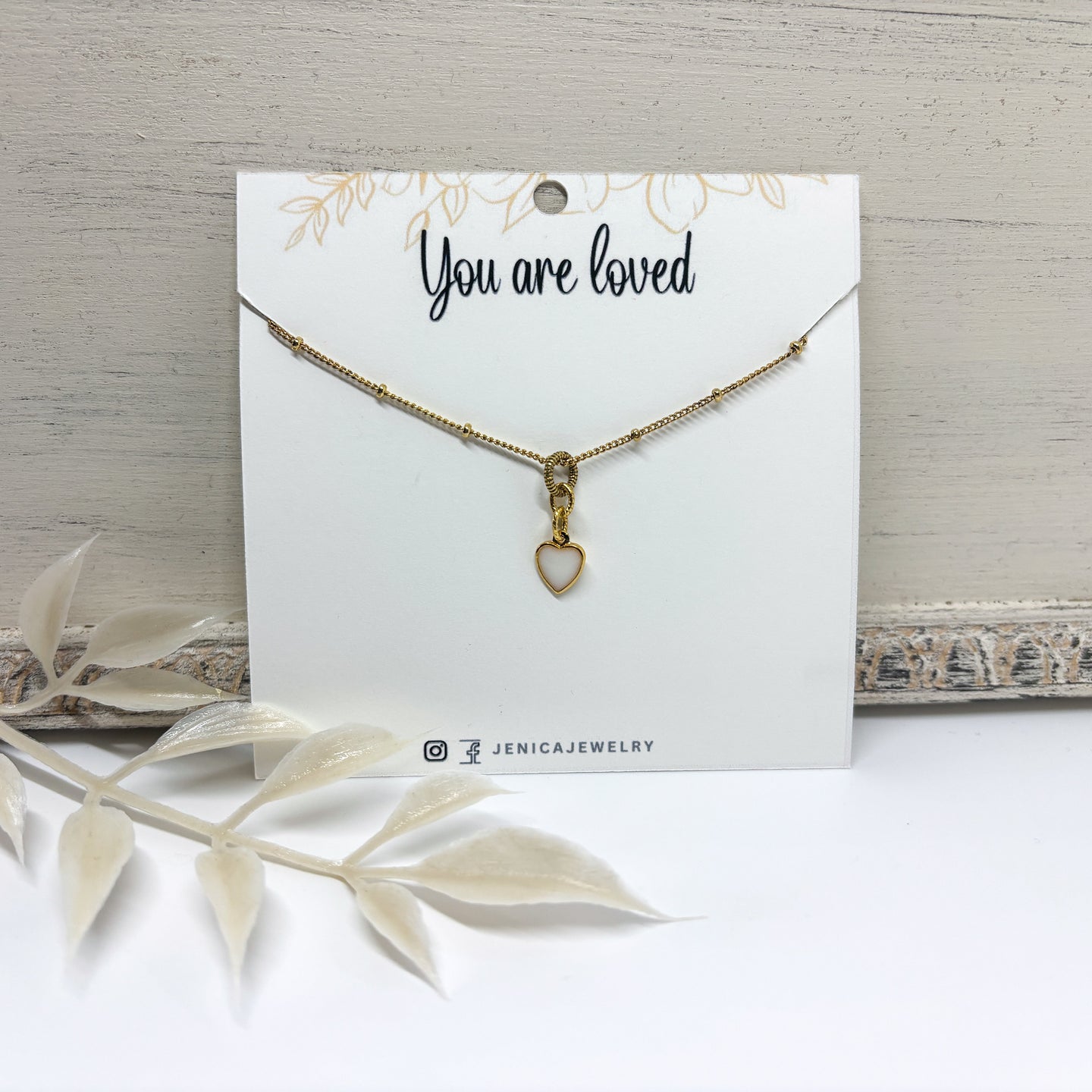 Itsy gold heart necklace with a resin filled white center on a card with 'You are loved'