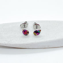 Pair of vibrant multicolor teardrop stud earrings displayed on a white textured ceramic dish against a clean white background. These handmade resin jewelry pieces feature a sparkling mix of magenta, gold, and teal faux druzy flakes in a classic teardrop shape with hypoallergenic silver posts. Perfect as everyday minimalist jewelry or unique handmade gifts for her.