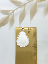 Silver tear shaped bezel on a gold ruler showing it measures 1" in length. Surrounding dried floral elements add a soft, natural composition.
