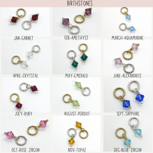 Product guide titled "Birthstones" displaying a 3x4 grid of crystal charm options for each month, each available with a gold or silver twisted jump ring:   Jan-Garnet: Deep red   Feb-Amethyst: Purple   March-Aquamarine: Light blue   April-Crystal: Clear   May-Emerald: Dark green   June-Alexandrite: Light purple   July-Ruby: Magenta   August-Peridot: Light green   Sept-Sapphire: Deep blue   Oct-Rose Zircon: Pink   Nov-Topaz: Amber   Dec-Blue Zircon: Aqua blue