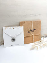 The necklace is on a white card with gold floral accents at the top, with a paper covering wrapped around it & stamped with Jenica's logo on the outside. It is finished with a simple string tied around it, making this necklace adorable for gift giving and easy to recycle.