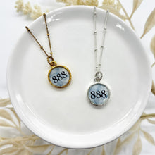 Round resin-sealed 888 angel number necklaces in gold and silver settings with a blueish background. 888 represents abundance and financial prosperity and that you are on the path to success.
