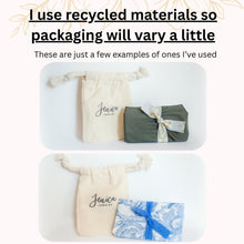An informational graphic explaining eco-friendly packaging. At the top, text reads: "I use recycled materials so packaging will vary a little. These are just a few examples of ones I’ve used." Two photos show cream-colored cotton drawstring pouches branded with "Jenica Jewelry" in script. One pouch is paired with a gift wrapped in olive green fabric and a patterned gold ribbon; the other is paired with a blue and white floral fabric wrap tied with a matching blue textured rib