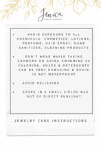 A jewelry care instructions card titled "Jenica JEWELRY & DESIGNS" with gold botanical line art at the top. Within a dotted border, bullet points advise avoiding chemical exposure, removing jewelry while showering or swimming, avoiding polishing, and storing in a small, sealed bag out of direct sunlight. Below the card, text reads "JEWELRY CARE INSTRUCTIONS".