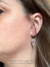 A close-up side profile of a person wearing a dainty, silver-framed heart-shaped earring with a shimmering crushed-stone finish.