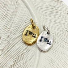 May include: Two oval-shaped metal charms with the words "I love you" engraved on them. One charm is gold and the other is silver.