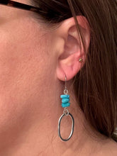 A model wearing a silver and turquoise chip drop earring. The jewelry showcases a modern geometric design with vibrant blue accents, highlighting the scale and fit of the earring against the ear and jawline.