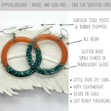 Infographic for hypoallergenic resin hoop earrings showing orange and dark teal dangles. Features text highlighting surgical steel posts and rubber stoppers, nickel and lead-free materials for sensitive ears. Over 2.5 inches long, these lightweight statement earrings contain "Glitter Roxs" translucent glass flakes. Available in silver or gold with gift ready packaging, perfect for boho jewelry lovers seeking unique, handmade accessories.