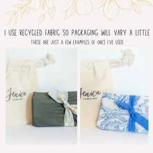 Eco-friendly jewelry packaging examples for Jenica Jewelry. Includes recycled fabric gift wrap in olive green with a gold chevron ribbon and a blue floral pattern with a lace tie. A branded drawstring cotton pouch is shown alongside the sustainable, plastic-free gift wrapping. Text explains that packaging varies due to the use of recycled materials, perfect for eco-conscious gifting and unique, handmade presents.