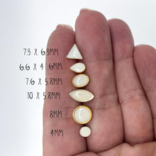 A size comparison of various white resin stud earrings held against a hand for scale. The image features six different geometric shapes in 24K gold plated settings, including triangle (7.3 x 6.mm), teardrop (6.6 x 4.6mm), oval (7.6 x 5.8mm), marquise (10 x 5.8mm), and two round sizes (8mm and 4mm). These minimalist geometric studs are perfect for second piercings or everyday wear. Handmade jewelry size guide for scale and variety.