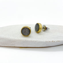 Handmade charcoal gray glitter resin stud earrings with a modern-vintage gold bezel. A pair of round 8mm minimalist studs rests on a white textured surface, showcasing one earring from the front and one from the side with its surgical steel post and butterfly clutch. The dark gray glass flakes catch the light inside the high-shine resin inlay, creating a subtle shimmer ideal for sensitive ears.
