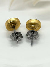 A close-up view focusing on the backs of a pair of handmade round stud earrings resting on a white surface. The image highlights the texture of the 24k gold-plated bezel backings, straight surgical steel posts and butterfly clutch backings securely attached to each earring. A soft, out-of-focus background keeps the emphasis directly on the hypoallergenic components.