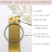 An infographic showing a large hammered hoop earring placed next to a brass ruler to measure its size. Text details include: lightweight, a little over 2.5 inches long, and 50mm (1.96 inches) wide. It notes surgical steel posts with rubber stoppers and options for 24K gold plated or .999 fine silver plated metal. A top banner highlights that the jewelry is hypoallergenic, nickel and lead-free, and safe for sensitive ears. Gift-ready packaging is included.