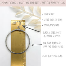 An infographic showing a large hammered hoop earring placed next to a brass ruler to measure its size. Text details include: lightweight, a little over 2.5 inches long, and 50mm (1.96 inches) wide. It notes surgical steel posts with rubber stoppers and options for 24K gold plated or .999 fine silver plated metal. A top banner highlights that the jewelry is hypoallergenic, nickel and lead-free, and safe for sensitive ears. Gift-ready packaging is included.