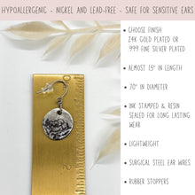 An infographic graphic features a silver stamped floral dangle earring on a brass ruler next to product specs.  A top banner reads "Hypoallergenic - Nickel and Lead-Free - Safe for Sensitive Ears." Bullet points note a choice of 24K gold or .999 fine silver plating, almost 1.5 inches in length, .70 inches in diameter, ink-stamped and resin-sealed, lightweight, surgical steel ear wires, and rubber stoppers.