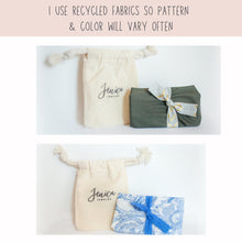 An informational graphic showcasing eco-friendly packaging options for jewelry. The image features a cream-colored drawstring pouch branded with "Jenica Jewelry" alongside small packages wrapped in recycled fabrics. The top example shows a solid olive green fabric tied with a gold-patterned ribbon, while the bottom example displays a blue and white floral fabric tied with a matching blue lace ribbon. Text at the top notes that recycled fabrics are used, so patterns and colors will vary