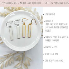 A graphic showing two pairs of dangle earrings in a small white dish. One pair features silver-bordered rectangular bars with white resin inlay & surgical steel ear wires with rubber stoppers. The other pair features identical bars with gold-borders & gold surgical steel ear wires.

Text on the right lists product features: lightweight, a choice of .999 fine silver plated or 24K gold plated finish resin filled bars, surgical steel wires, 1.75" length, resin-filled bars, and gift-ready packa