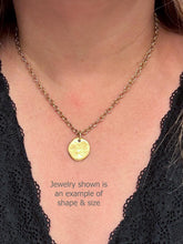 A model wearing a gold cable chain necklace featuring a small, organic round charm with a wax-seal style. Below the pendant, grey overlay text reads, "Jewelry shown is an example of shape & size". The model is dressed in a black lace-trimmed top against a neutral background.