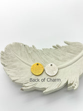 Two small, round metal charms—one gold and one silver—resting on a textured white decorative feather tray against a plain white background. Both blank charm backs feature a textured, slightly rustic finish and a small hole near the top. Grey text overlaying the feather below the charms reads "Back of Charm".